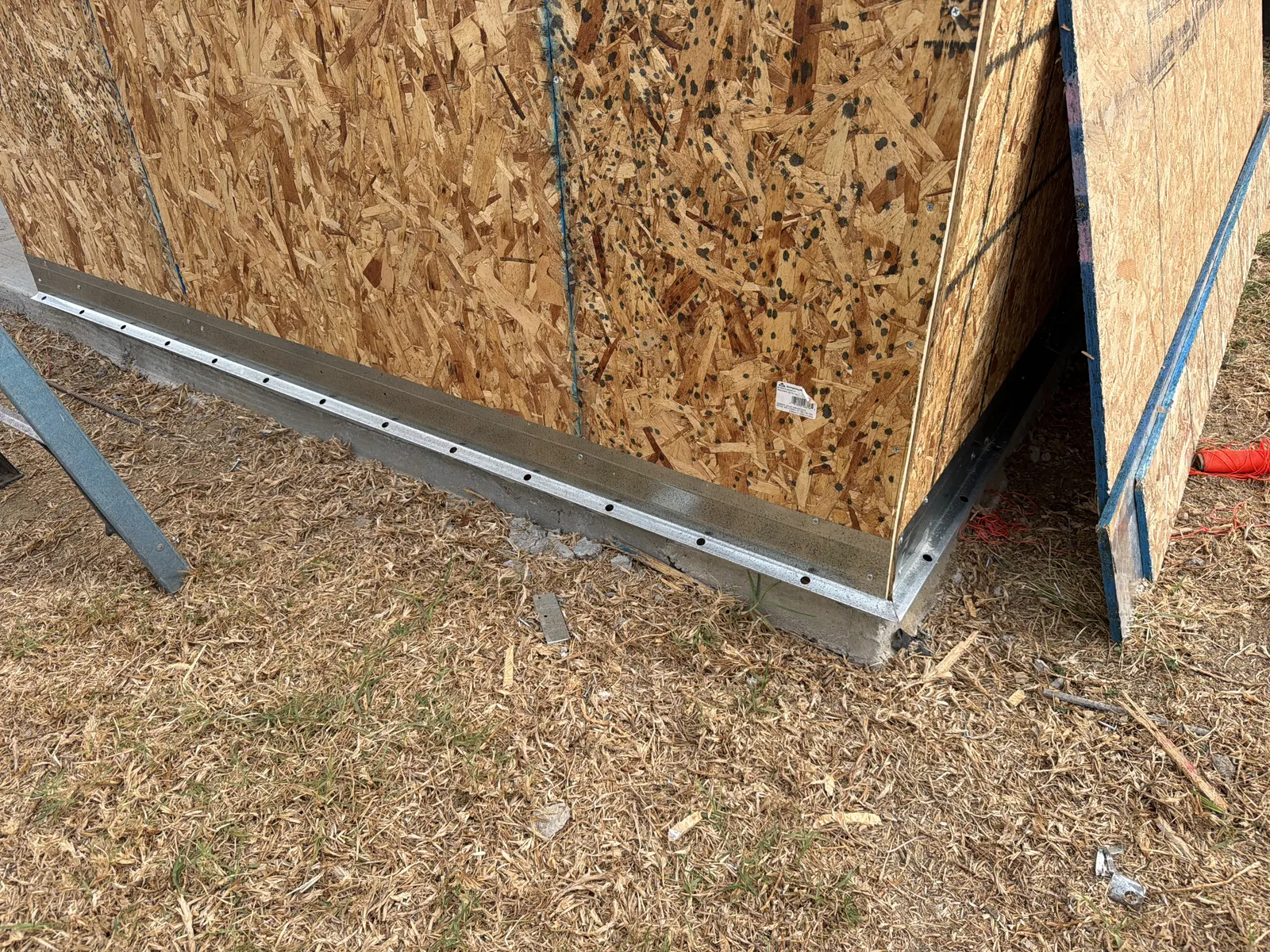 Close-up of the sheathed wall base, metal base trim, and concrete slab edge during construction
