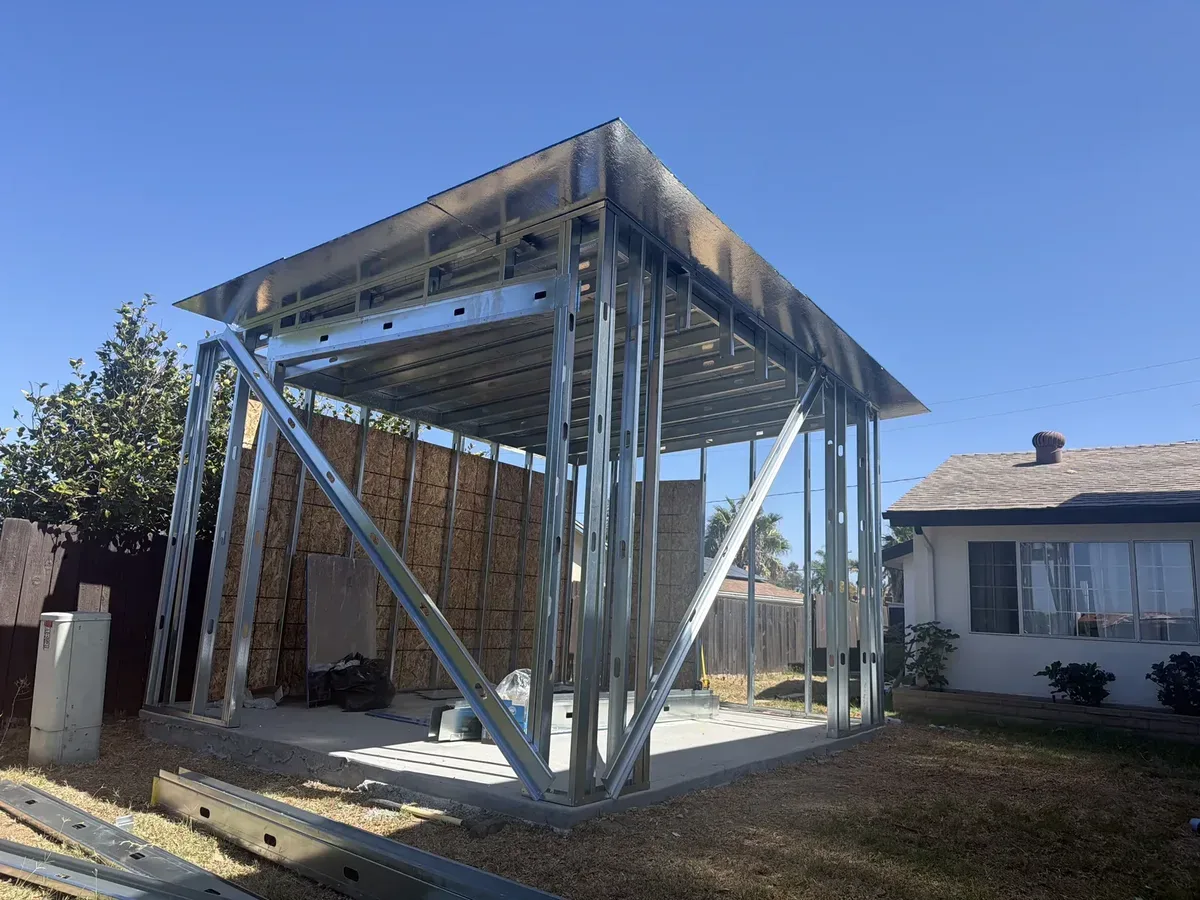 Metal roof framing spanning an unfinished open structure with wall framing and partial sheathing